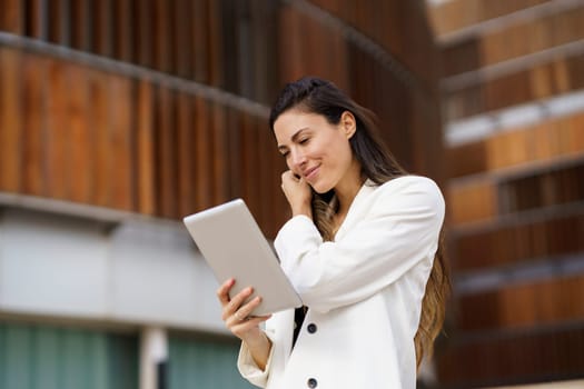 A confident woman in a stylish white blazer interacts with her tablet, showcasing modern technology in an elegant environment