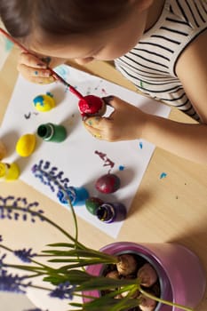 Little child girl paint Easter eggs at home. kid is preparing for Easter.