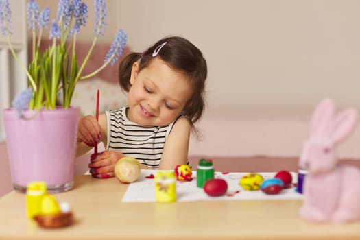 Little child girl paint Easter eggs at home. kid is preparing for Easter.