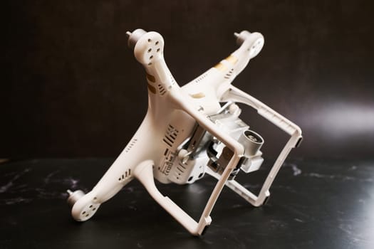 White drone without propellers DJI Phantom 3 lies on its side on stands on a black table. High quality photo