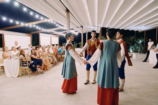 Group of Montenegrins in national costumes sing, holding hands in a circle on stage in front of applauding guests. High quality photo