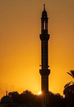 Minaret of a Mosque silhouetted against brilliant sunset sky along Nile River in Egypt