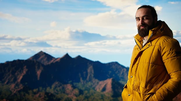 Hiker dressed in warm clothing stands on a mountain peak after climbing to the top, gazing at the breathtaking landscape of rugged hills and vast sky. Adventure with scenic view. Camera A.