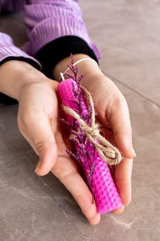 Caucasian female hands holding pink beeswax candle with dried flowers and twine.