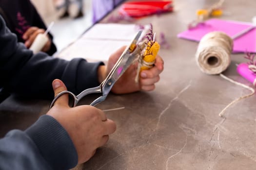 Young caucasian child crafting with scissors and yarn on a table.