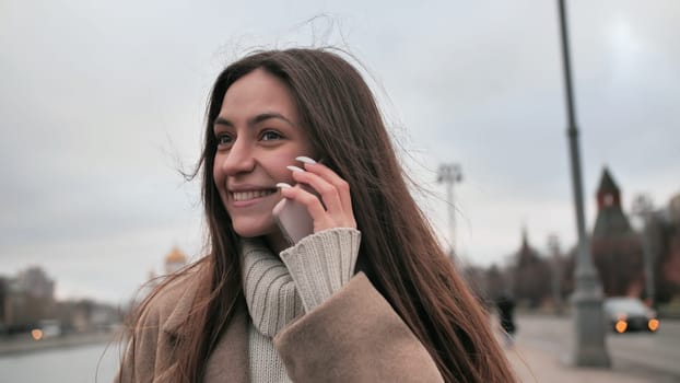 Happy young girl talking on the phone while walking along the street in Moscow. A girl calls a taxi on the phone