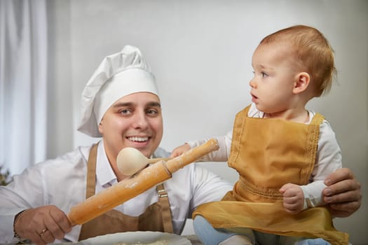 A family enjoys a fun cooking session, playfully covered in flour while engaging with their little ones in a warm kitchen. Father and son having fun