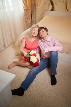 A middle-aged couple poses together in a hotel room, sharing smiles and holding flowers while celebrating their love.