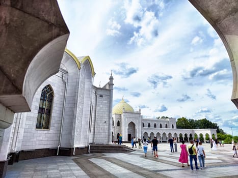 Bolgar, Russia - August 04, 2024: People admire the intricate design and beauty of the White Mosque in Bolgar, surrounded by lush greenery and spacious grounds.