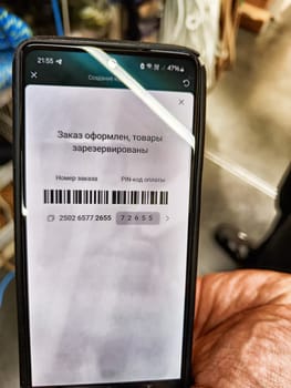 Kirov, Russia - February 05, 2025: A user holds a mobile device showing an order confirmation with a barcode and reservation details in a retail environment.