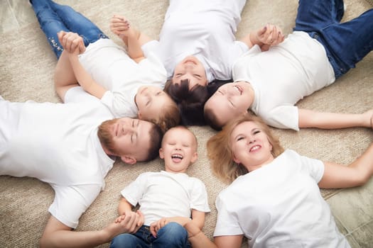 Group of six family members share a joyful moment on a soft rug, smiling and laughing together in a comfortable home setting.
