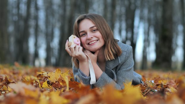 A young beautiful girl takes pictures in an autumn park using a toy camera