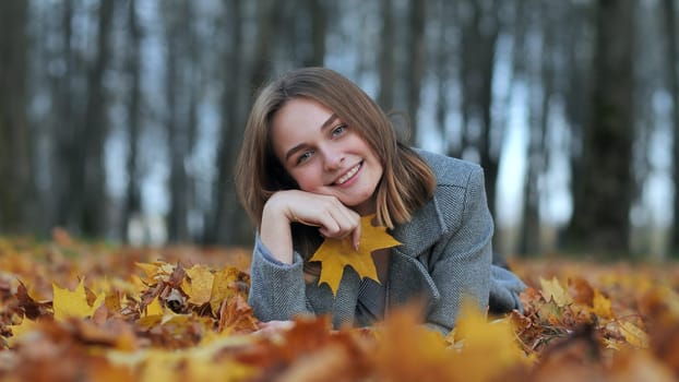 Beautiful happy young girl with a smile holds an autumn yellow leaf near the face