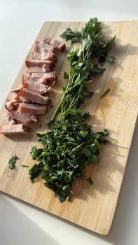 Sliced Smoked Lard and Fresh Parsley on Wooden Cutting Board. A close-up shot of a wooden cutting board with freshly chopped parsley and sliced smoked lard (salo). The sunlight highlights the textures and colors of the ingredients, creating a warm and rustic atmosphere. A perfect setup for traditional Eastern European cuisine.