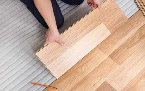 Installing laminated floor, detail view from above on man hands holding wooden tile, fitting it, over white foam base layer