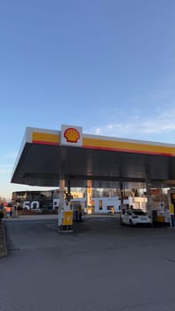 22.03.2025 Germany: Modern Gas Station Shell With Logo Sign at Sunset. A contemporary Shell gas station with logo branding under a clear evening sky, showcasing a white parked car and various fueling pumps, set in an urban environment with adjacent buildings.