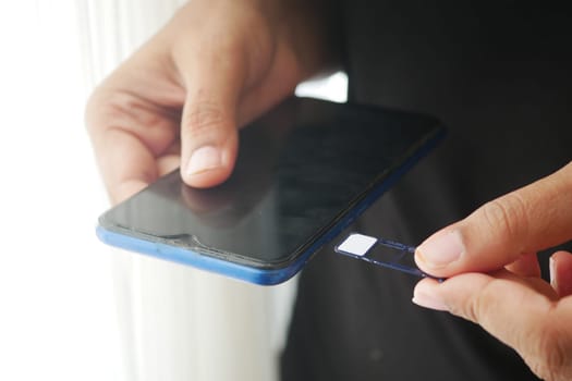 A person is removing a SIM card from a smartphone while sitting in light.
