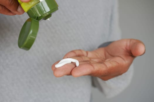 A person dispenses cream onto their hand for skincare application.