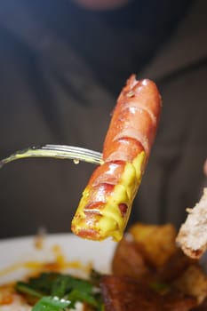 Diners savor a grilled sausage topped with mustard and served with bread.