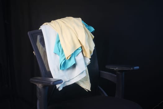 Colorful casual clothes lie on an office chair against a dark backdrop.