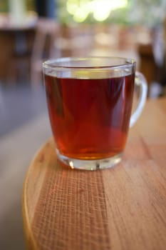 A clear cup filled with dark herbal tea rests on a wooden table.