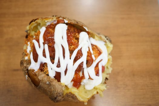 A baked potato overflowing with chili, sour cream, and toppings on a table.