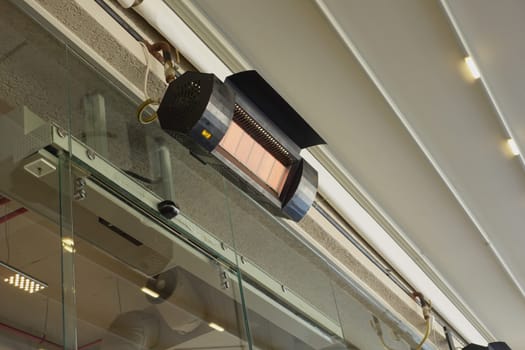 A heating unit is suspended above a glass panel, providing warmth indoors.