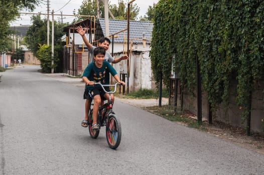 Two happy friends of teenage boy ride a bike during summer holidays in Kazakhstan. Shymkent, Kazakhstan - July 12, 2024