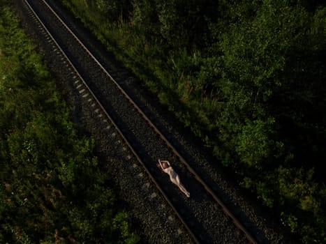 Top view of naked female in lying on rail road at sunrise