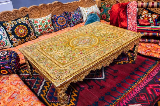 beautiful patterned traditional Uzbek dastarkhan table, colorful pillows and a vintage carpet in the interior of a house in Uzbekistan. Life and culture of Central Asia