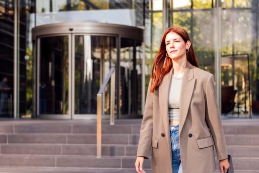 young adult woman in casual suit walking in front of an office building holding a briefcase, concept of entrepreneur and business, copyspace for text