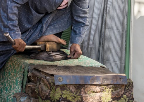 A tailor skillfully uses a foot-operated iron to smooth material in Esna, Egypt, showcasing traditional tailoring techniques