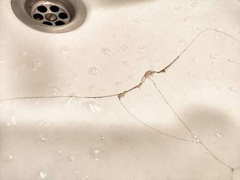 A noticeable crack runs through the surface of the sink, accompanied by water droplets that highlight the damage.