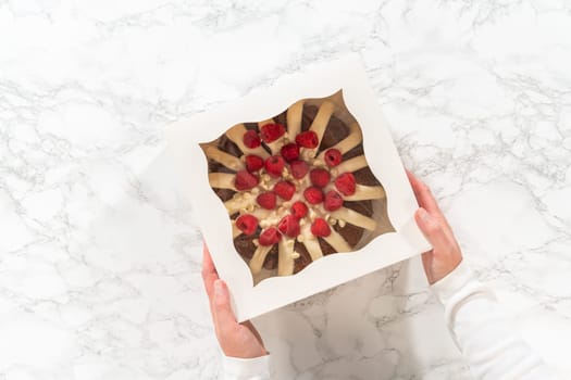 Flat lay. With care, the White Chocolate Raspberry Bundt Cake is packaged into a white paper box - ready for gifting to bring joy and indulgence to someone special.