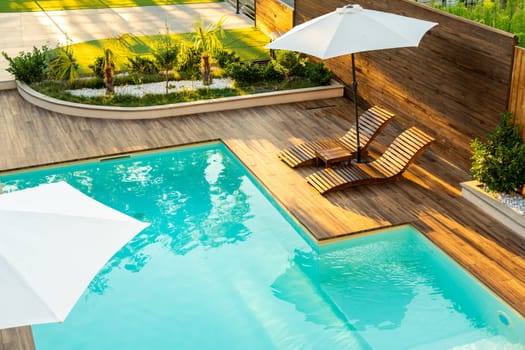 Elegant turquoise swimming pool with wooden deck, lounge chairs, and umbrellas in a sunny backyard