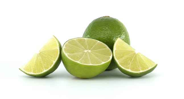 One whole lime fruit stands behind two lime quarters and a lime half, showcasing the vibrant green color and juicy texture of the citrus fruit against a clean white backdrop