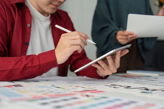 A designer is focused on a digital interface with a tablet in hand, working alongside her team on refining UIUX elements.
