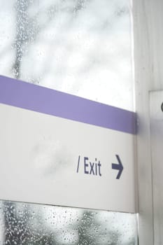 Sign directing people to the exit with raindrops on the glass.