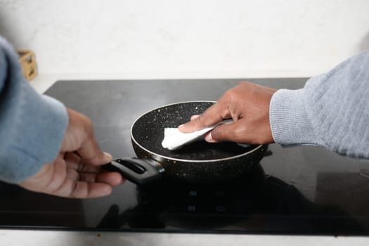 A person wipes a frying pan on an induction cooktop while cooking.