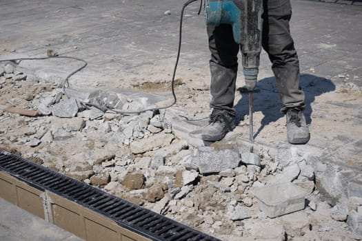 A construction worker operates a jackhammer on broken pavement during a project.