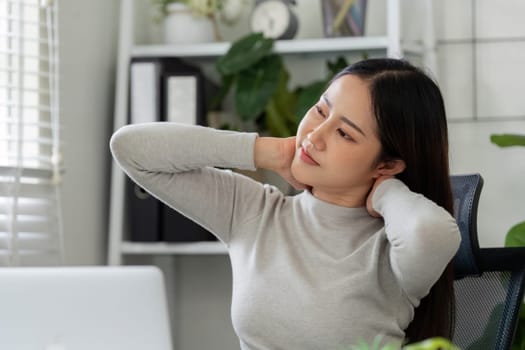 Taking a moment to stretch, the woman addresses her neck discomfort during a work session, balancing productivity with well-being in her home environment.