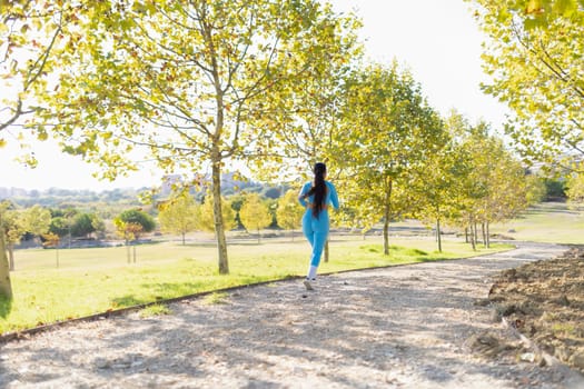 Young sportswoman running in a park during a sunny autumn day