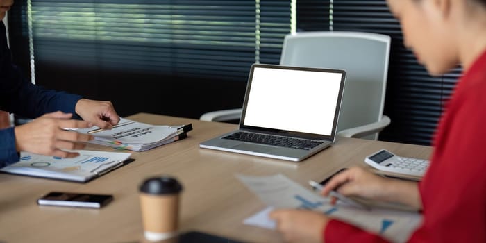 In a stylish office, colleagues are deeply engrossed in reviewing financial reports alongside digital devices, fostering a collaborative environment for decision-making.