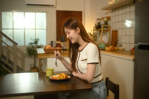 Happy young woman enjoying a delicious breakfast in a cozy home kitchen.