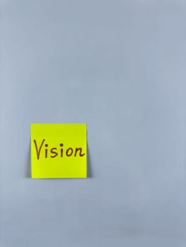 Sticky note with Vision written on it, affixed to white background. Photo represents foresight and goals, ideal for themes of vision and future aspirations