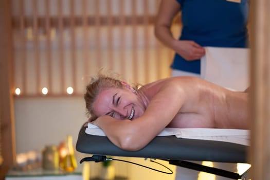 Relaxing Back Massage in a Spa Setting. A professional massage therapist in a blue uniform provides a relaxing back massage to a client lying on a massage table