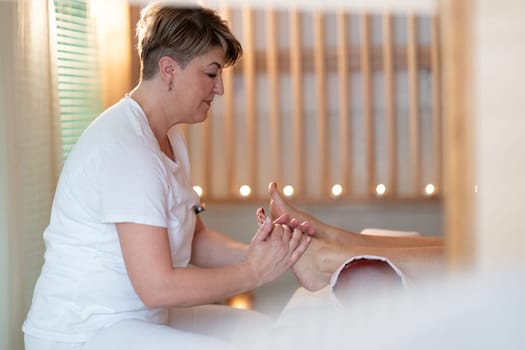 A professional massage therapist in a white uniform provides a soothing foot massage to a client in a calm and serene spa environment.