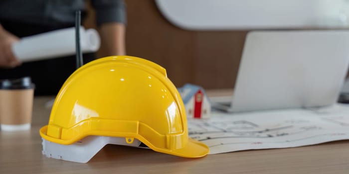 A bright yellow hard hat lies on a desk filled with architectural plans and blueprints, emphasizing safety and careful planning in the engineering process.