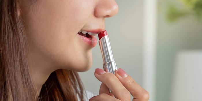 With a precise motion, the woman glides red lipstick on her lips, completing her glamorous look with confidence.