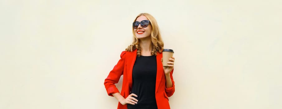 Stylish happy young woman in business suit, red blazer jacket with cup of coffee looking away standing on white studio background